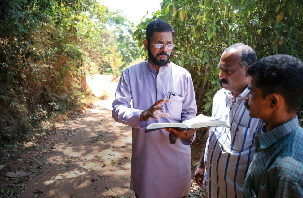 Indian Pastor Beaten by RSS Mob, Attackers Come to Christ a man reads the bible to two other men outside