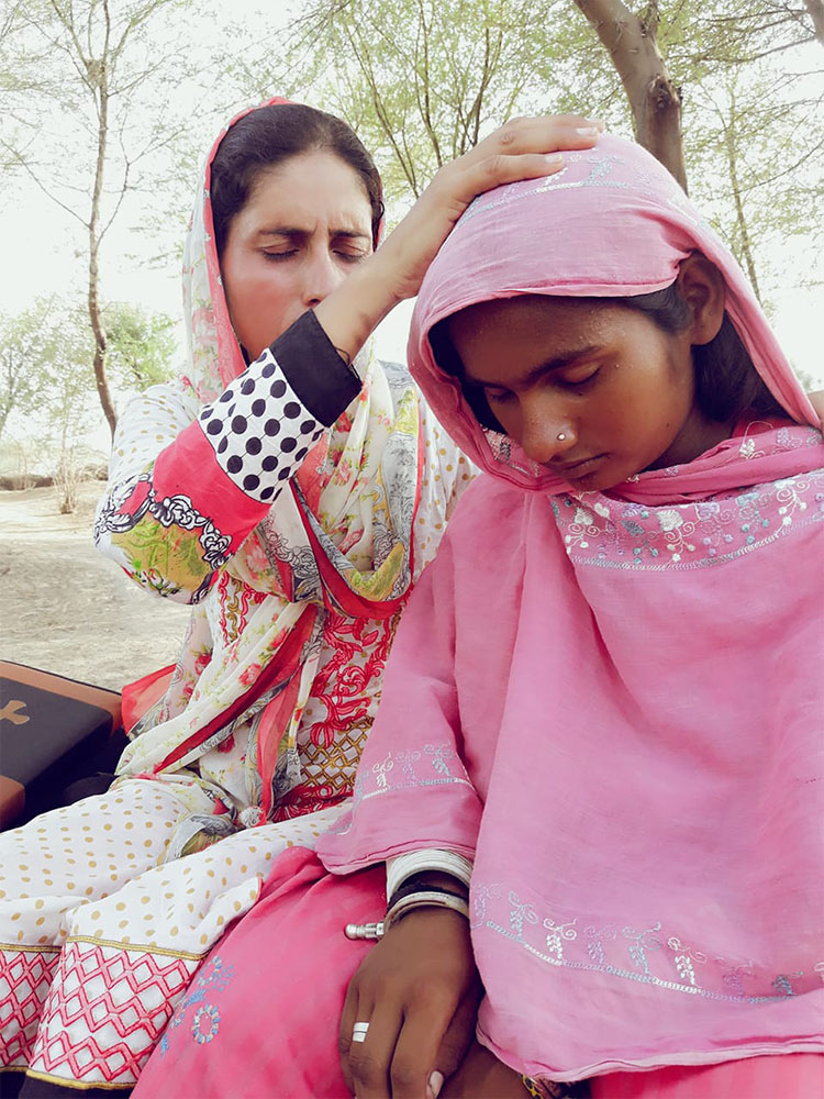 Woman with praying with hand on head of girl